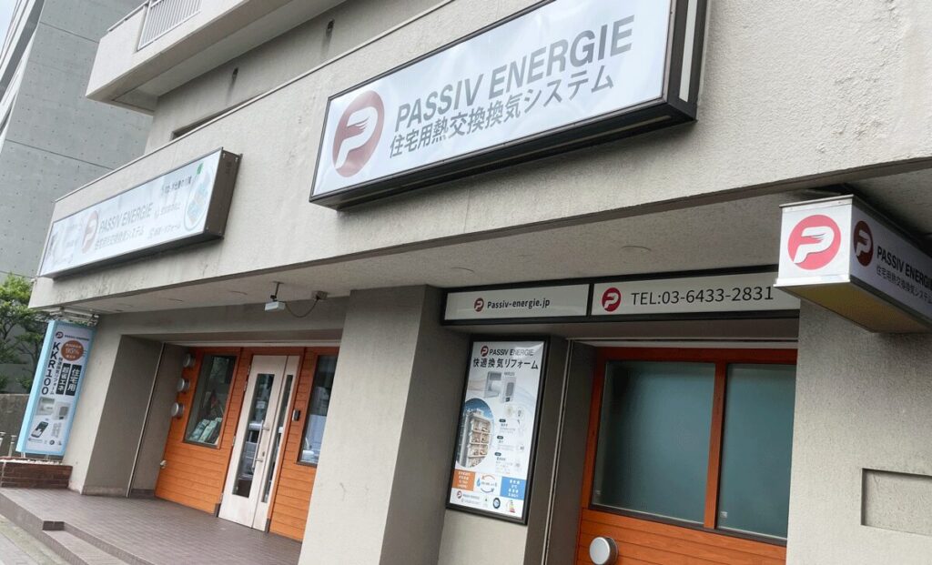 「PASSIV ENERGIE」のロゴ看板と、ダクトレス熱交換換気システム「せせらぎ」の製品看板が掲げられたオフィスの外観・入り口の様子